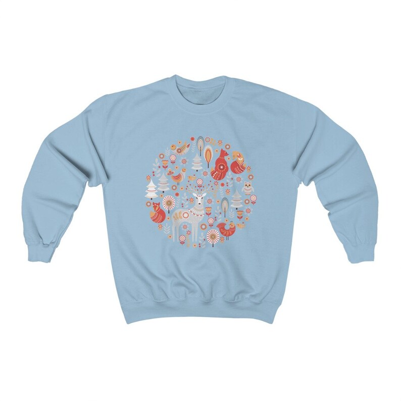 May include: Light blue sweatshirt with a circular design featuring a deer, foxes, birds, trees, and flowers in red, orange, and white on a light blue background.