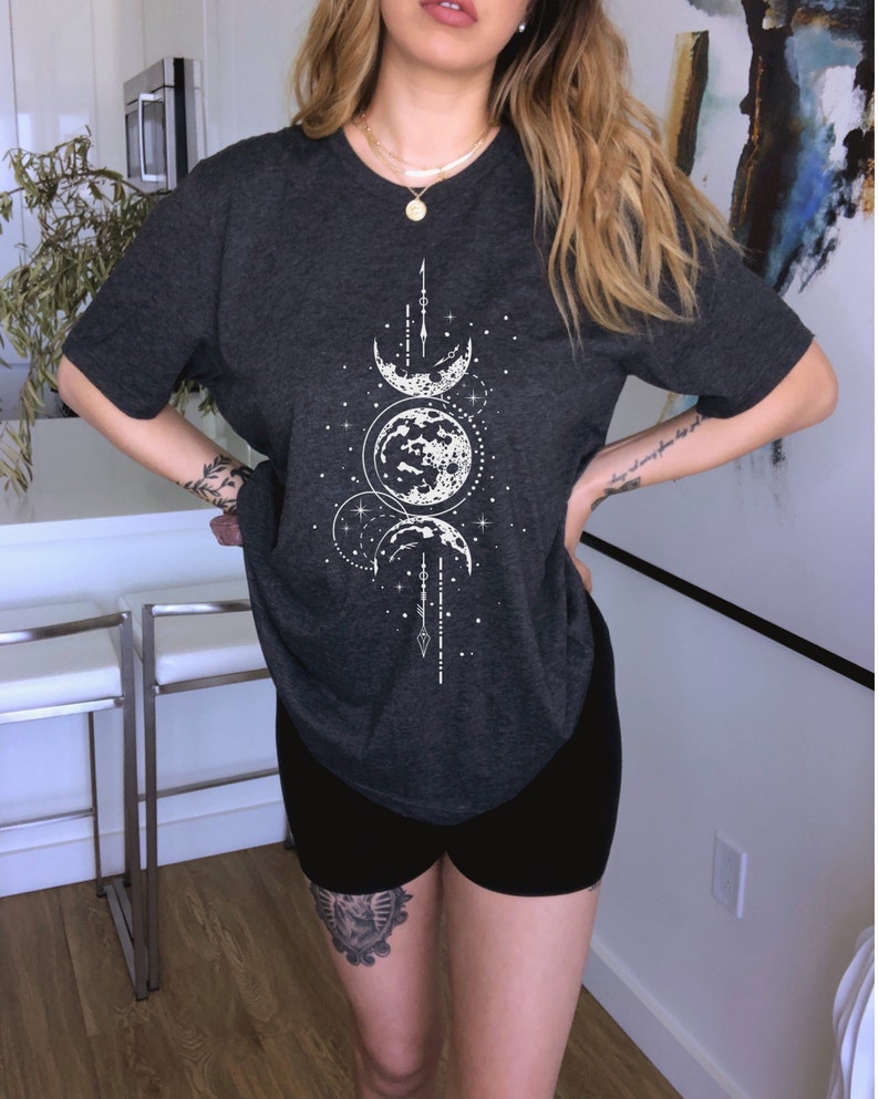May include: A dark gray t-shirt with a white moon and stars graphic. The shirt has a relaxed fit and a round neckline.