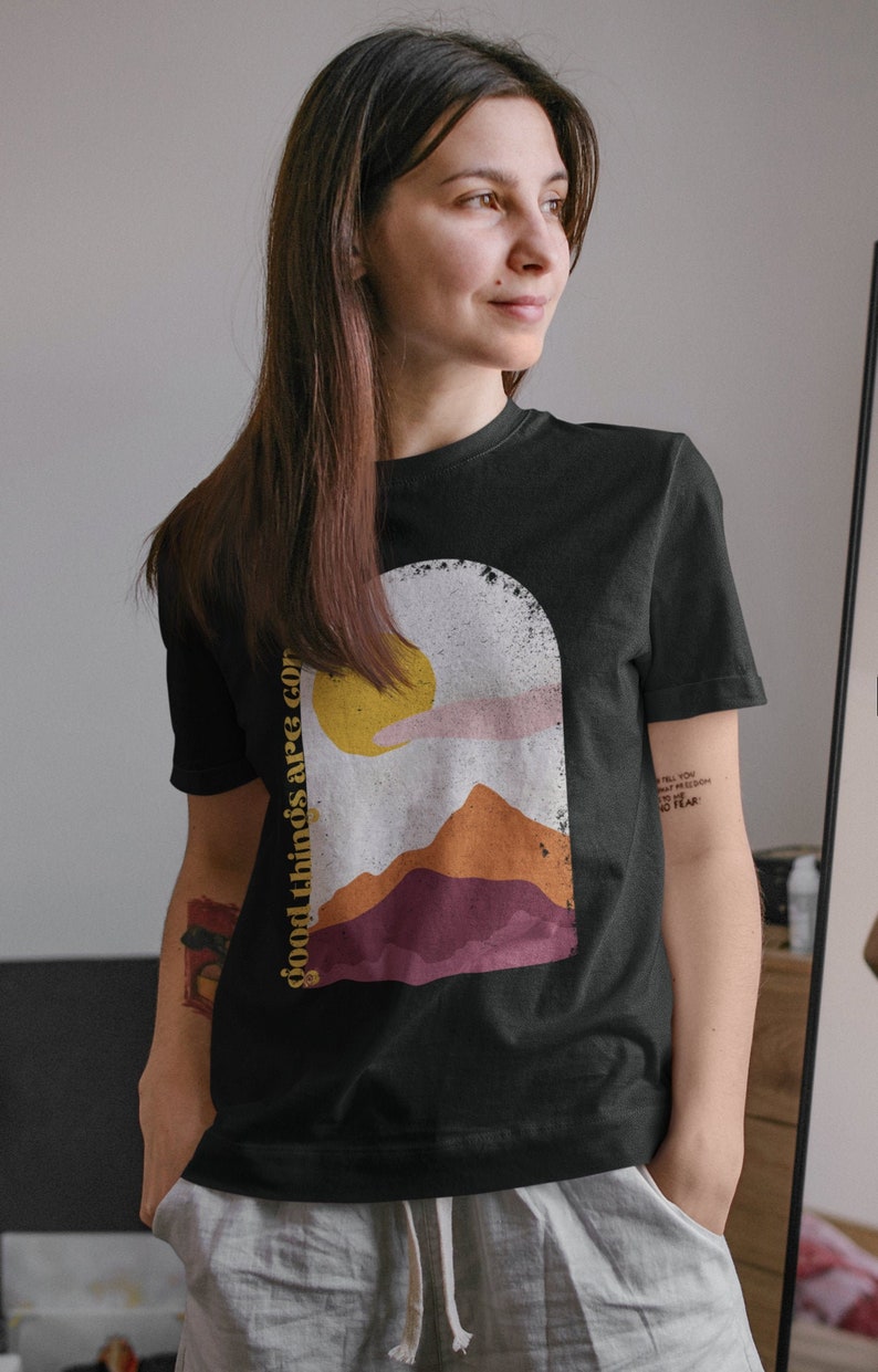 Puede incluir: Camiseta negra con un gr&aacute;fico de una puesta de sol sobre monta&ntilde;as y el texto "good things are coming".