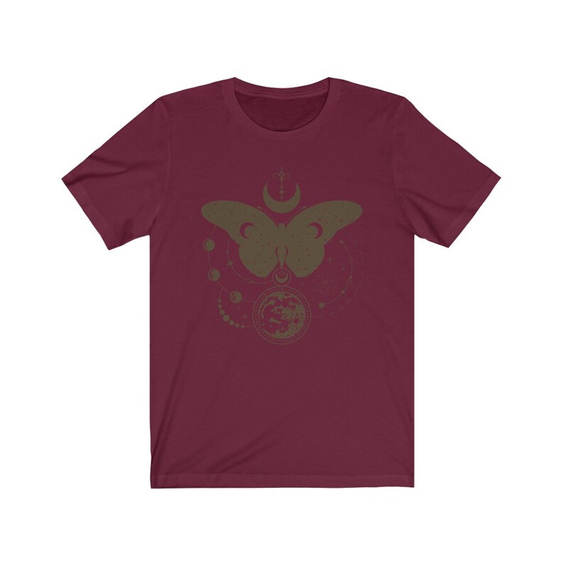 May include: A maroon short-sleeved t-shirt with a graphic print of a butterfly with a crescent moon and stars. The butterfly is in a dark green color.