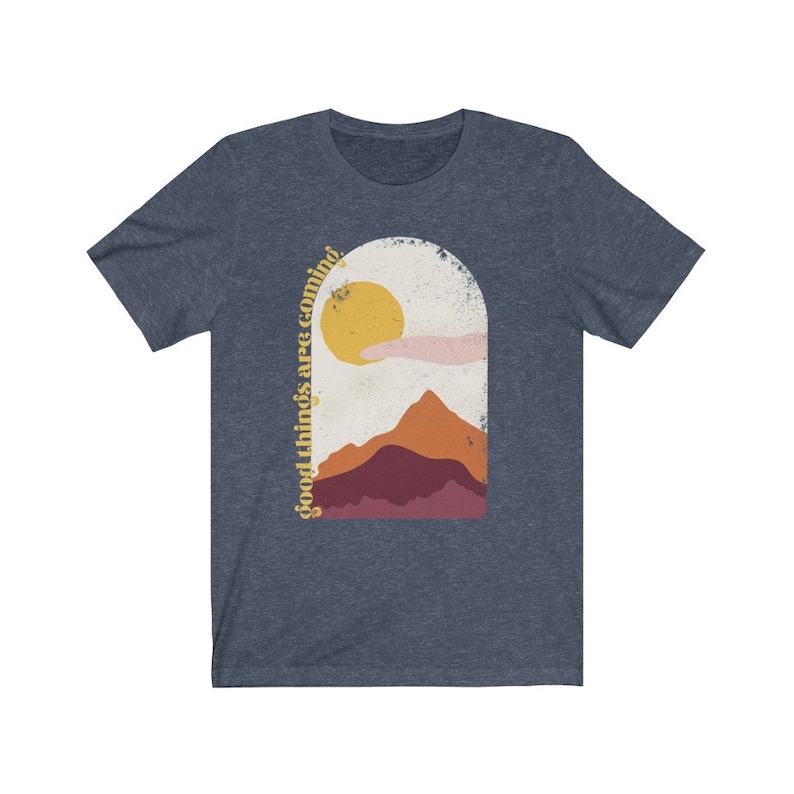 Puede incluir: Una camiseta azul marino con un gr&aacute;fico de una cordillera, un sol y una mano extendida. El texto "good things are coming" est&aacute; escrito verticalmente en el lado izquierdo del gr&aacute;fico.