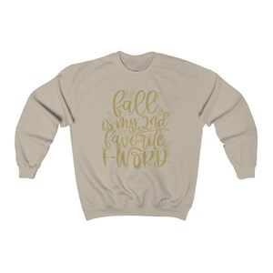 May include: A beige sweatshirt with the text "fall is my 2nd favorite f-word" in gold lettering.