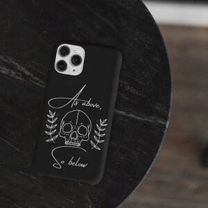 Op de afbeelding: Zwarte telefoonhoes met een witte schedel en een bloemenontwerp. De tekst "As above, so below" is op de hoes gedrukt.
