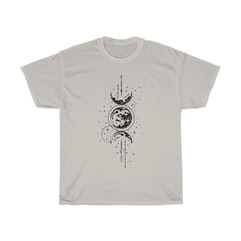 May include: A light gray t-shirt featuring a black graphic of the phases of the moon. The design includes crescent moons, a full moon, stars, and lines. The shirt is made of a soft material.