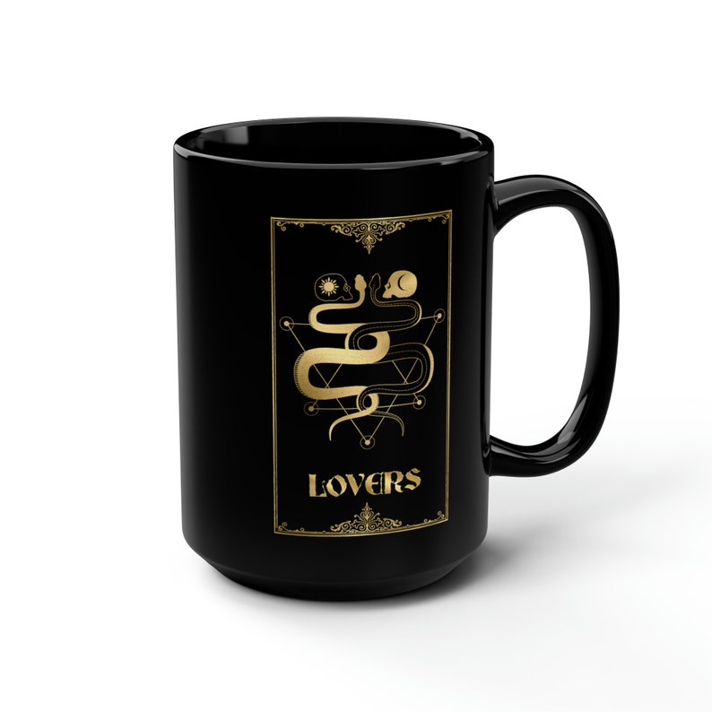 Puede incluir: Taza de caf&eacute; de cer&aacute;mica negra con un dise&ntilde;o dorado de dos serpientes entrelazadas alrededor de un pentagrama con la palabra "LOVERS" en letras doradas.
