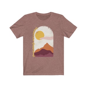 Puede incluir: Una camiseta de color gris jaspeado con un gr&aacute;fico de un sol, monta&ntilde;as y el texto "good things are coming".