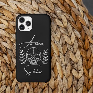 Op de afbeelding: Zwarte telefoonhoes met een witte schedel en bloemenontwerp. De tekst "As above, so below" staat op de hoes.