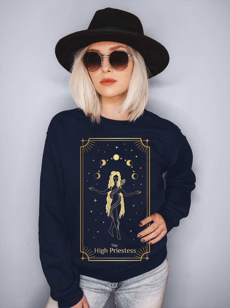 Op de afbeelding: Een marineblauw sweatshirt met een gouden afbeelding van de Hogepriesteres tarotkaart. De kaart toont een vrouw met een slang om haar heen, die voor een halve maan en sterren staat.