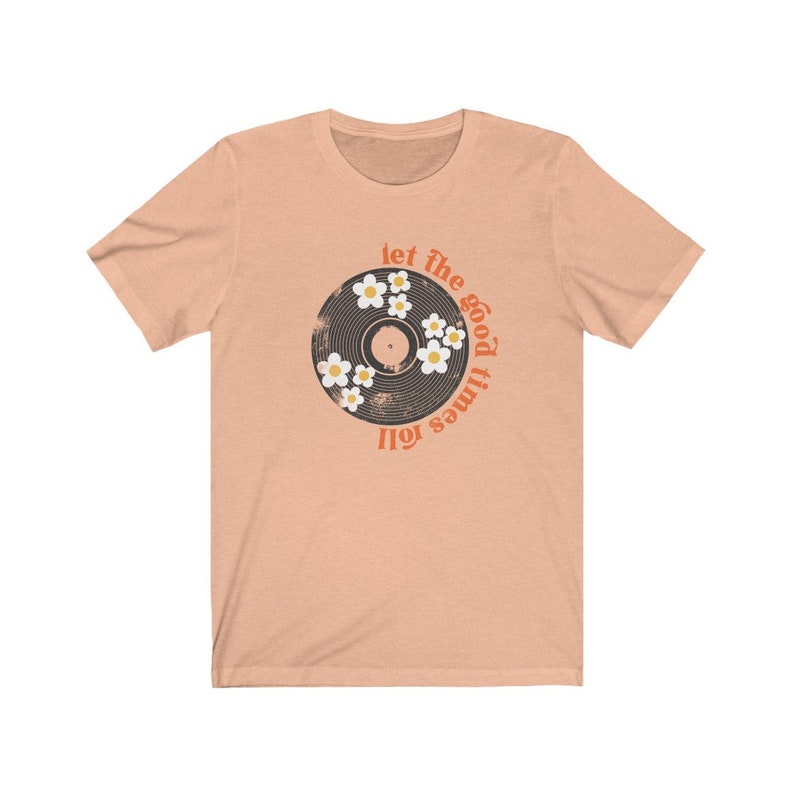 K&ouml;nnte beinhalten: Ein pfirsichfarbenes T-Shirt mit einem Vintage-Schallplatten-Design mit wei&szlig;en G&auml;nsebl&uuml;mchen und dem Text "Let the good times roll."