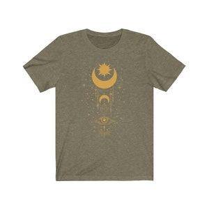 May include: A green t-shirt with a gold design of a crescent moon, sun, and eye with geometric shapes and stars.