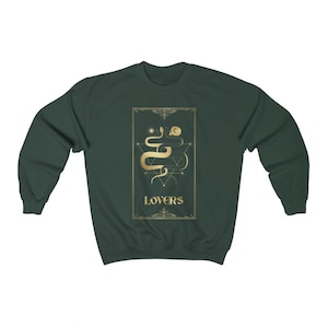 Puede incluir: Una sudadera de color verde oscuro con un dise&ntilde;o dorado de una serpiente y la palabra "LOVERS" en la parte delantera.
