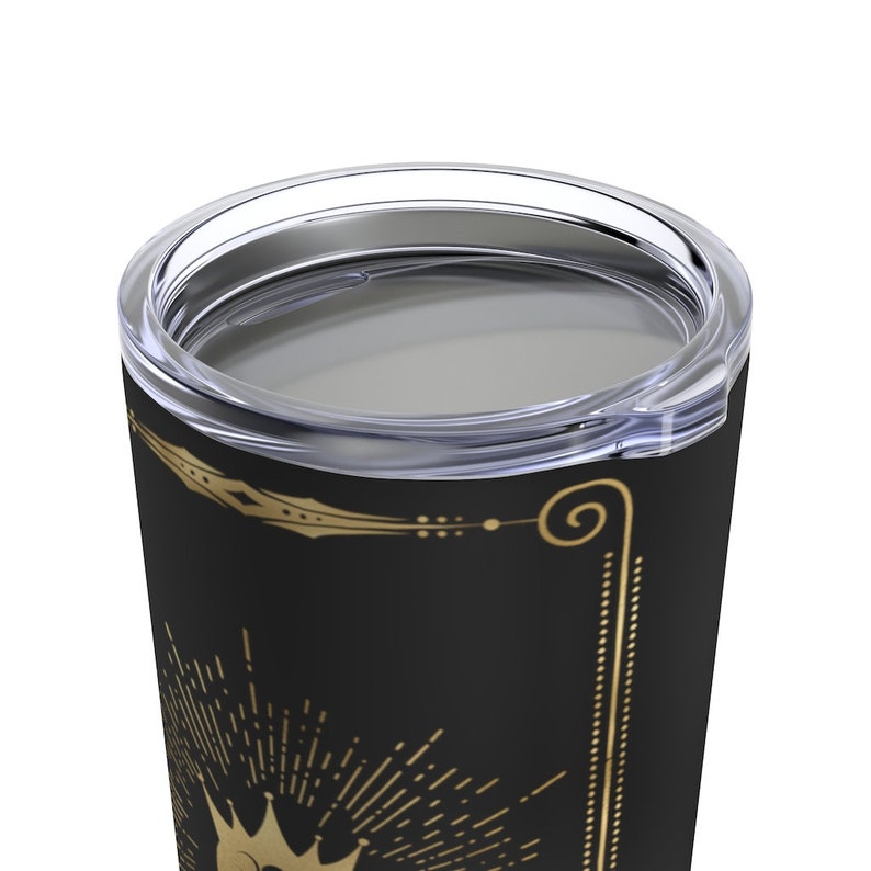May include: A black stainless steel tumbler with a gold crown and sunburst design. The tumbler has a clear lid.