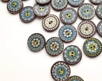 May include: Assortment of wooden buttons with blue, green, and brown mandala designs. The buttons are scattered on a white surface.