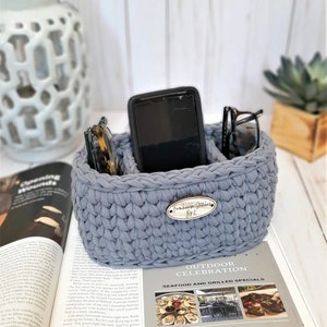 Puede incluir: Un organizador de crochet gris con tres compartimentos para guardar objetos como un tel&eacute;fono, gafas u otros objetos peque&ntilde;os. El organizador tiene una etiqueta de madera que dice "Farmhouse Gather Bok".