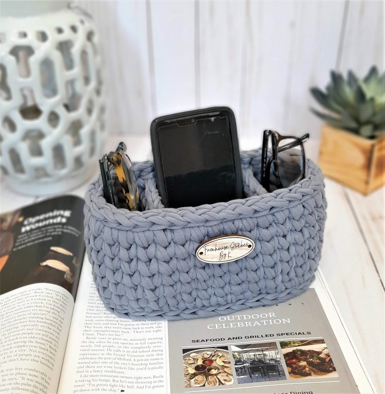 Puede incluir: Un organizador de crochet gris con tres compartimentos para guardar objetos como un tel&eacute;fono, gafas u otros objetos peque&ntilde;os. El organizador tiene una etiqueta de madera que dice "Farmhouse Gather Bok".