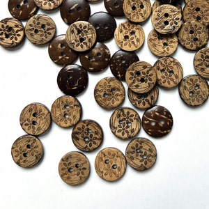 May include: A collection of brown and natural coconut shell buttons with intricate floral designs. The buttons are scattered on a white surface.