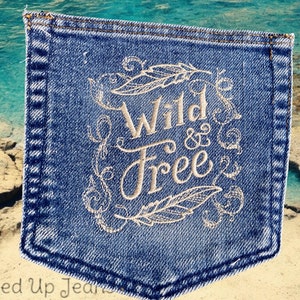 May include: A close-up of a blue denim pocket with white embroidery that reads "Wild & Free" surrounded by stylized leaves and feathers.