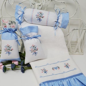 May include: A set of four white and blue embroidered sachets and a white hand towel with blue trim. The sachets are filled with dried lavender and have a floral design. The towel has a floral design and a heart.