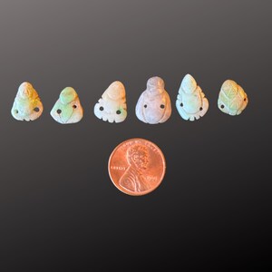 Puede incluir: Seis peque&ntilde;as tallas de jade verde de una criatura m&iacute;tica con dos agujeros a cada lado. Las tallas est&aacute;n dispuestas en fila y tienen aproximadamente el tama&ntilde;o de una moneda de un c&eacute;ntimo de euro.