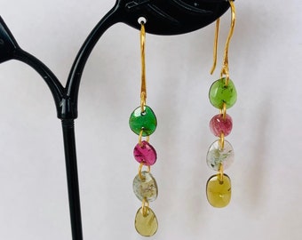 May include: Gold dangle earrings with a series of oval-shaped green, pink, and yellow gemstones.