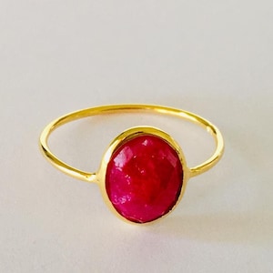 May include: A gold ring featuring a large, oval-shaped, bright pink gemstone.