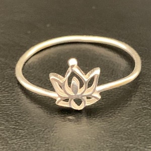 Può includere: Un anello d'argento con un delicato design a forma di fiore di loto. L'anello è semplice ed elegante, il che lo rende un accessorio perfetto per ogni occasione.