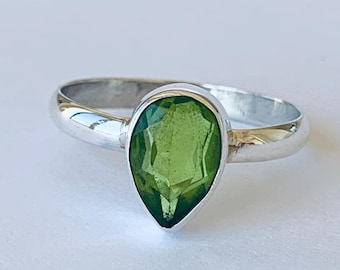 Op de afbeelding: Een zilveren ring met een peervormige groene edelsteen.