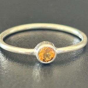 Könnte beinhalten: Ein silberner Ring mit einem kleinen, runden, orangefarbenen Edelstein.
