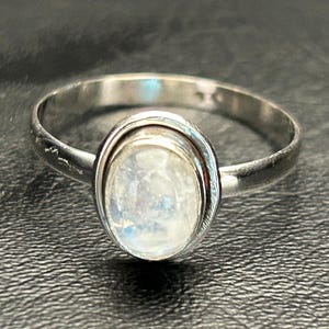 May include: A silver ring with a white oval moonstone set in a bezel setting.