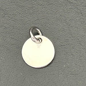 May include: A silver round charm with a smooth surface and a small loop at the top.