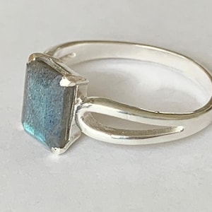 May include: A silver ring featuring a square-shaped blue labradorite gemstone. The ring has a simple, open band design.