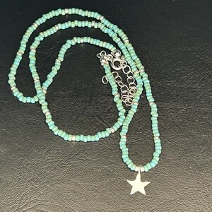 May include: A turquoise beaded necklace with a silver star charm. The necklace is made of small, round beads and is layered for a bohemian look.