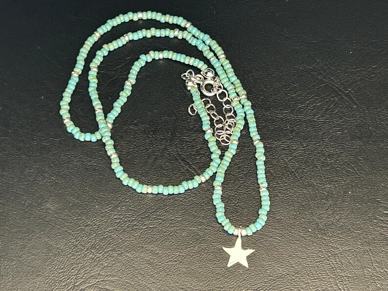 May include: A turquoise beaded necklace with a silver star charm. The necklace is made of small, round beads and is layered for a bohemian look.