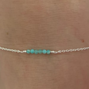 Könnte beinhalten: Ein zartes Armband aus Silberkette mit einer Reihe von hellblauen Edelsteinperlen.