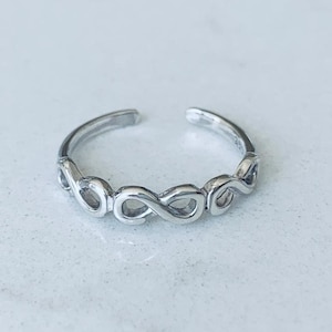Puede incluir: Un anillo de dedo del pie de plata con un delicado diseño de infinito.