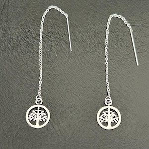 Könnte beinhalten: Ein Paar silberne Ohrhänger mit einem Lebensbaum-Motiv. Die Ohrringe bestehen aus einer dünnen Kette mit einem kleinen Kreis am unteren Ende. Das Lebensbaum-Motiv ist aus dem Kreis ausgeschnitten.
