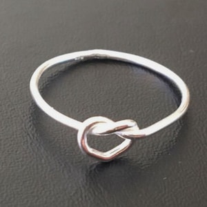May include: A silver ring with a knot design. The knot is shaped like a heart.