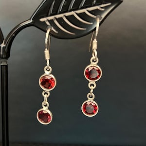 May include: Silver dangle earrings with three red gemstone accents.