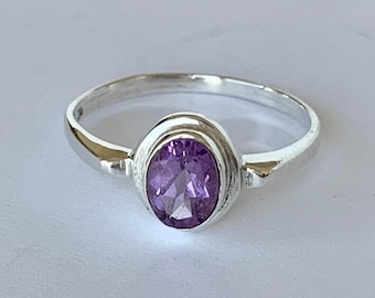 May include: A silver ring with a purple oval gemstone set in a bezel setting.