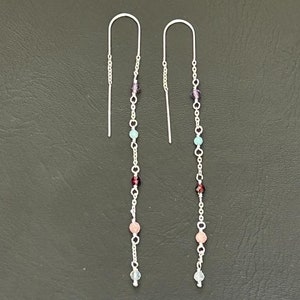 Könnte beinhalten: Ein Paar lange silberne Ohrringe mit einer Kette aus bunten Perlen. Die Perlen sind rosa, rot, blau und lila.