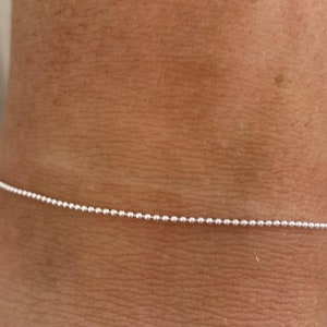 Peut inclure: Un bracelet délicat en argent avec une chaîne à boules. Le bracelet est composé de petites perles sphériques espacées régulièrement. La chaîne est présentée sur un fond de ton chair, soulignant ses détails fins et son design minimaliste.