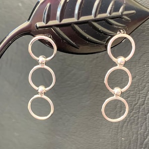 May include: A pair of silver hoop earrings with three rings and a bead on each earring.
