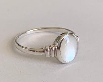 May include: A silver ring with a white oval-shaped gemstone. The ring has a simple design with a band that is slightly wider at the setting.