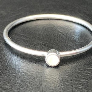 May include: A simple silver ring with a small, round, white stone in the center.