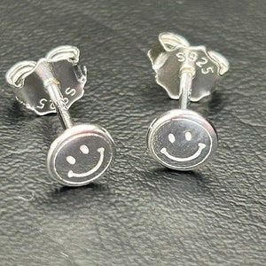 May include: A pair of silver smiley face stud earrings. The earrings are marked with "925" on the back.