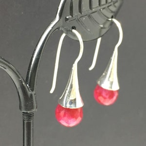 May include: A pair of silver dangle earrings with red gemstone drops. The earrings have a teardrop shape and are suspended from a silver hook.