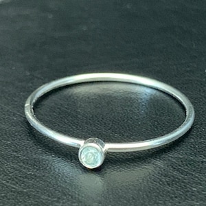 May include: A silver ring with a small, light blue gemstone.
