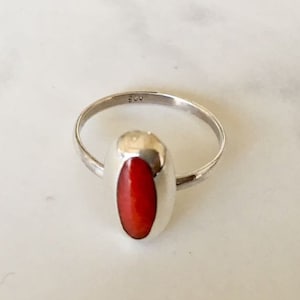 Pu&ograve; includere: Un anello d'argento con una pietra ovale rossa incastonata in una montatura a castone.