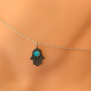 Könnte beinhalten: Ein silbernes Fußkettchen mit einem Hamsa-Hand-Anhänger mit einem blauen Opal-Stein.
