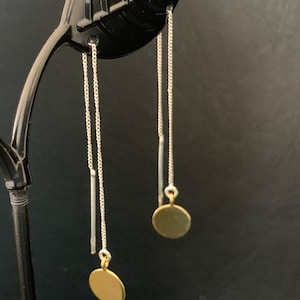 Puede incluir: Un par de pendientes de aro dorados con cadenas plateadas y una barra plateada que cuelga de cada pendiente.